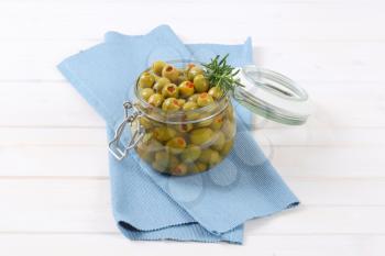 jar of green olives stuffed with red pepper on blue place mat