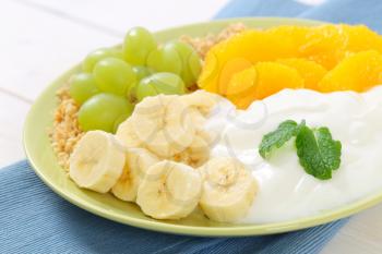 plate of muesli with white yogurt and fresh fruit on blue place mat - close up