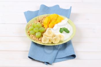 plate of muesli with white yogurt and fresh fruit on blue place mat