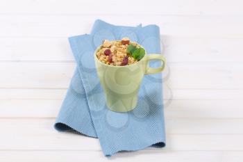 cup of granola with hazelnuts and dried cranberries on blue place mat