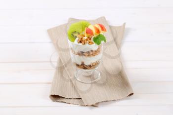 glass of muesli with yogurt and fresh fruit on beige place mat