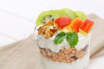 glass of muesli with yogurt and fresh fruit on beige place mat - close up