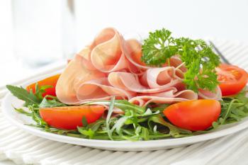 plate of fresh arugula leaves with sliced ham and halved tomatoes