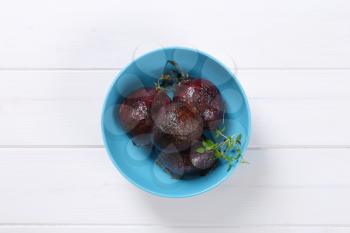 bowl of baked whole beetroots with thyme on white wooden background