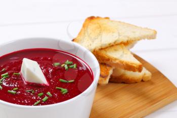 bowl of beetroot cream soup with toast on wooden cutting board - close up