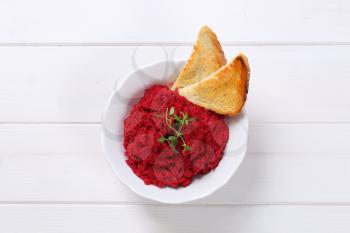 bowl of fresh beetroot puree with toast on white wooden background
