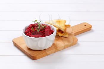 bowl of fresh beetroot puree with toast on wooden cutting board