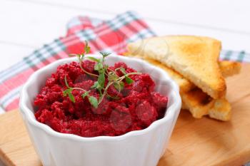 bowl of fresh beetroot puree with toast on wooden cutting board - close up