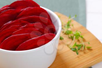 bowl of thin beetroot slices on wooden cutting board - close up