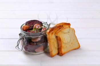 jar of baked beetroot and garlic with toasted bread on white wooden background