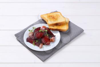 plate of baked beetroot and garlic with toasted bread on grey place mat