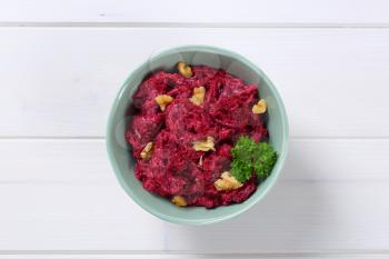 bowl of fresh beetroot spread with walnuts on white wooden background
