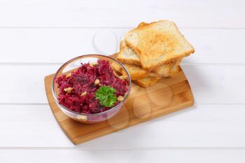 bowl of fresh beetroot spread with toast on wooden cutting board