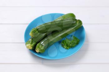 plate of fresh green zucchini on white wooden background