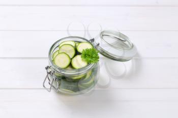 jar of green zucchini slices on white wooden background