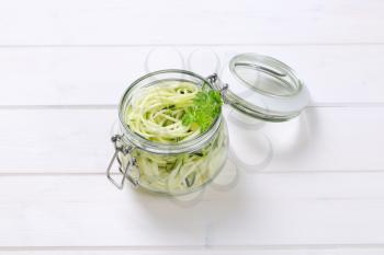 jar of raw zucchini noodles on white wooden background