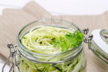 jar of raw zucchini noodles on beige place mat - close up