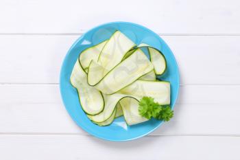 plate of raw zucchini strips on white wooden background