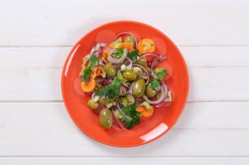 plate of vegetable salad with pickled green olives on white wooden background
