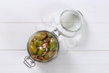 jar of marinated green olives on white wooden background