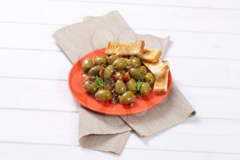 plate of marinated green olives with toast on beige place mat