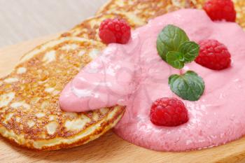 american pancakes with pink yogurt and fresh raspberries on wooden cutting board - close up