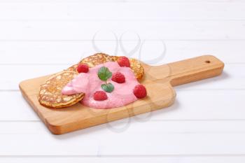 american pancakes with pink yogurt and fresh raspberries on wooden cutting board