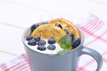 cup of american pancakes with white yogurt and fresh blueberries on checkered dishtowel - close up
