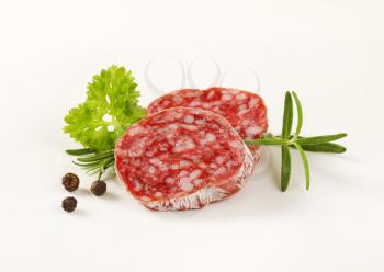 Slices of dry cured sausage with herbs and peppercorns on white background