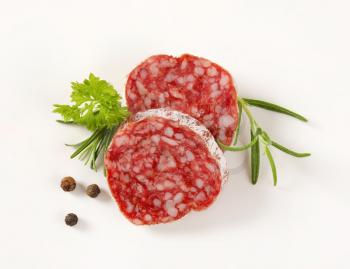 Slices of dry cured sausage with herbs and peppercorns on white background