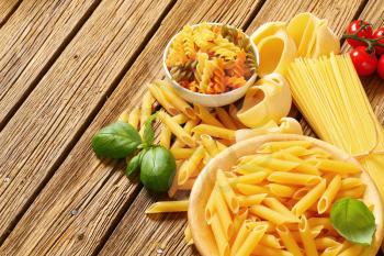 Various types of dried pasta on wooden background