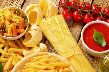 Assorted pasta and tomato passata on wooden background