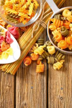 Various types of coloured pasta on a wooden background