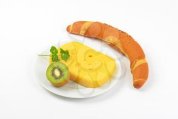 block of cheese, kiwi and fresh bread roll on white background