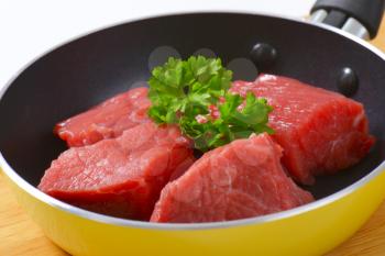 close up of diced raw beef meat with parsley in frying pan
