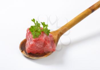 piece of raw beef meat with parsley on wooden spoon