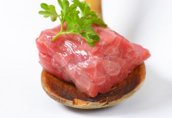 piece of raw beef meat with parsley on wooden spoon - detail