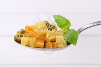 spoon of raw colored pasta on white wooden background