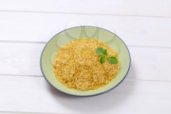 plate of dry wheat bulgur on white wooden background