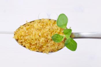 spoon of dry wheat bulgur on white wooden background