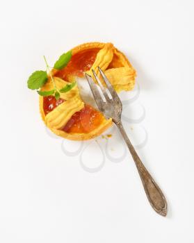 halved apricot jam tart and silver fork on white background