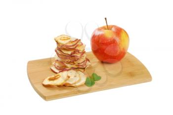 stack of dried apple chips and fresh apple on wooden cutting board