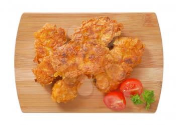 fried corn flake crusted chicken meat on wooden cutting board