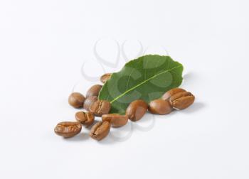 handful of roasted coffee beans with leaf on white background