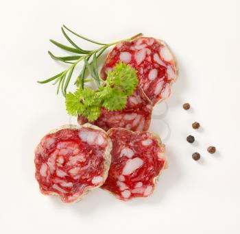slices of dry cured salami with spices on white background