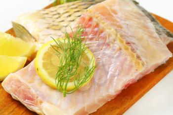 Raw carp fillets with lemon and dill on cutting board