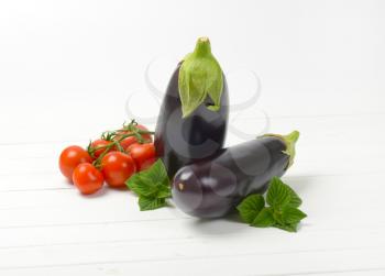 two fresh eggplants and tomatoes on white wooden background