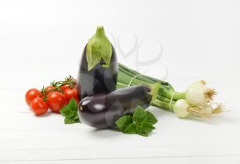 fresh eggplants, tomatoes and spring onion on white wooden background
