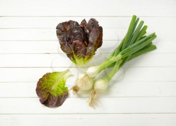 bunch of spring onions and head of fresh lettuce on white wooden background