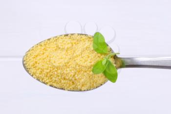 spoon of raw couscous on white wooden background